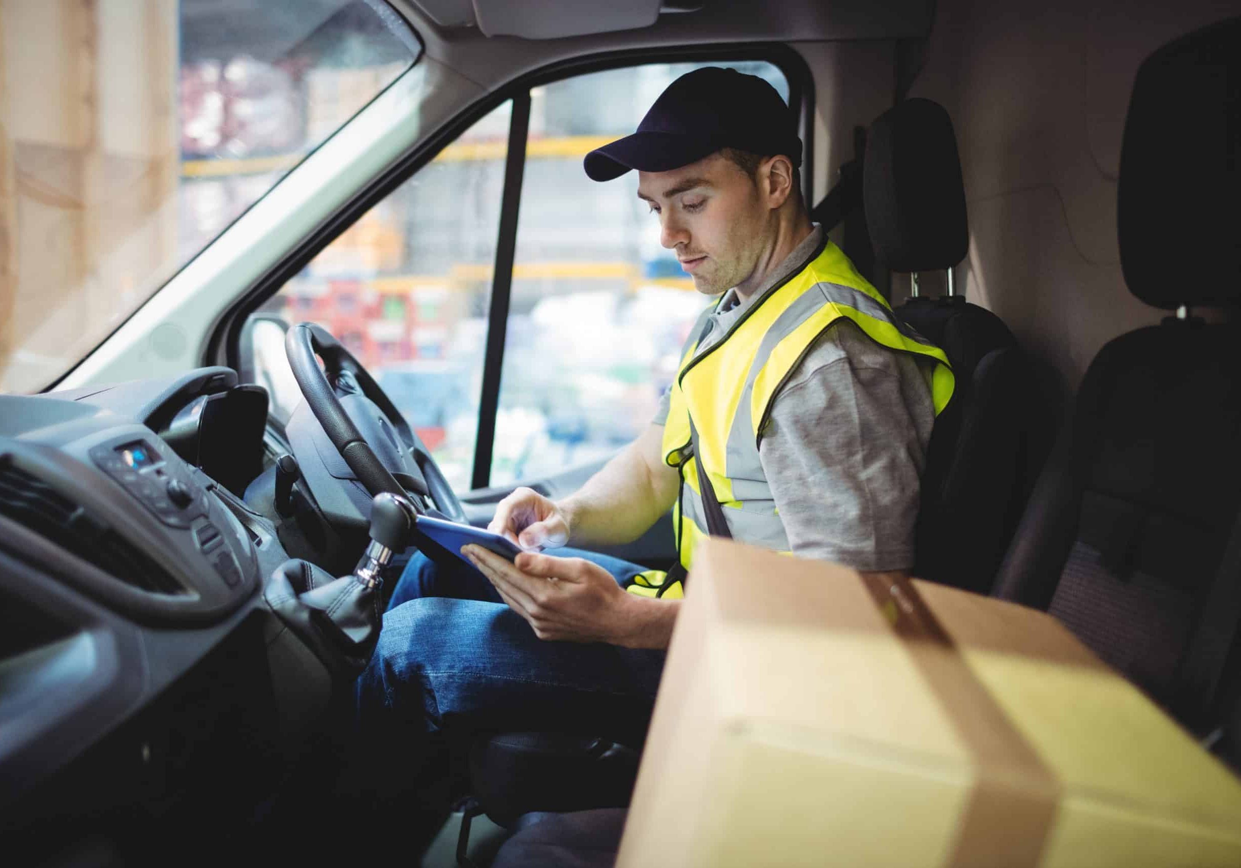 Delivery driver using tablet in van with parcels on seat express road freight deliver services
